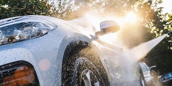 A white SUV being rinsed with water in bright sunlight