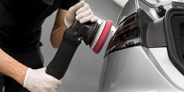 A technician polishing the rear quarter of a gray vehicle