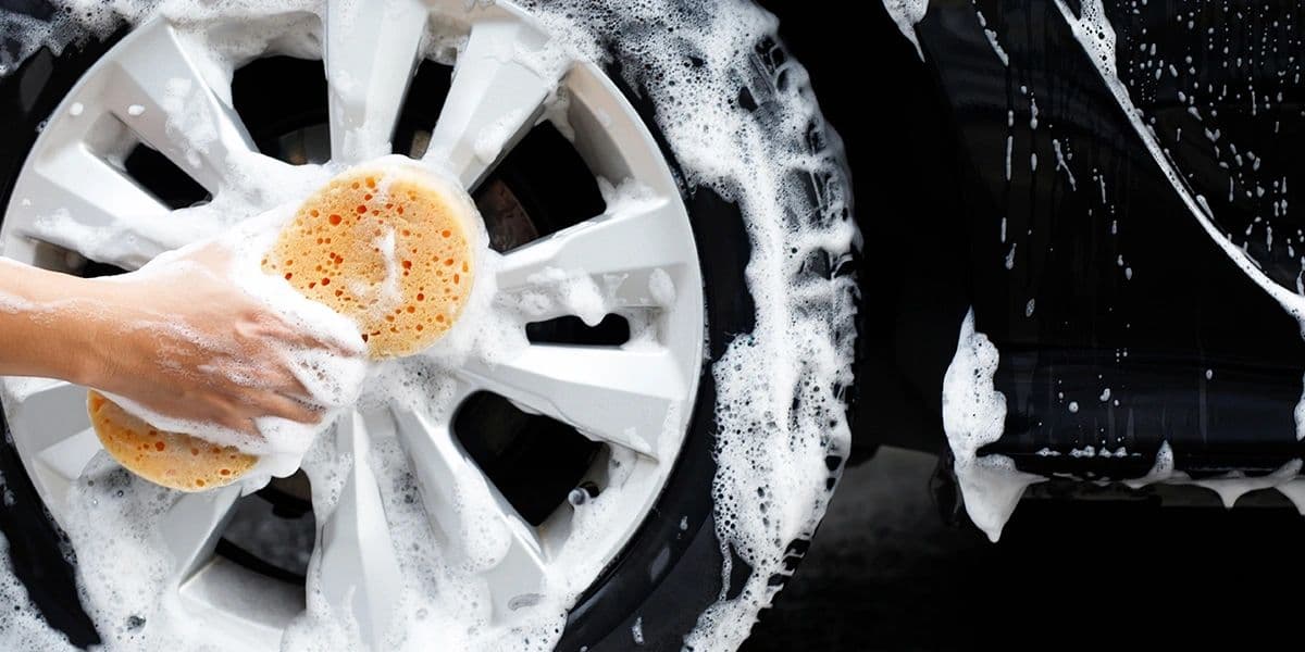 A vehicle wheel being carefully hand washed with a sponge and soap suds